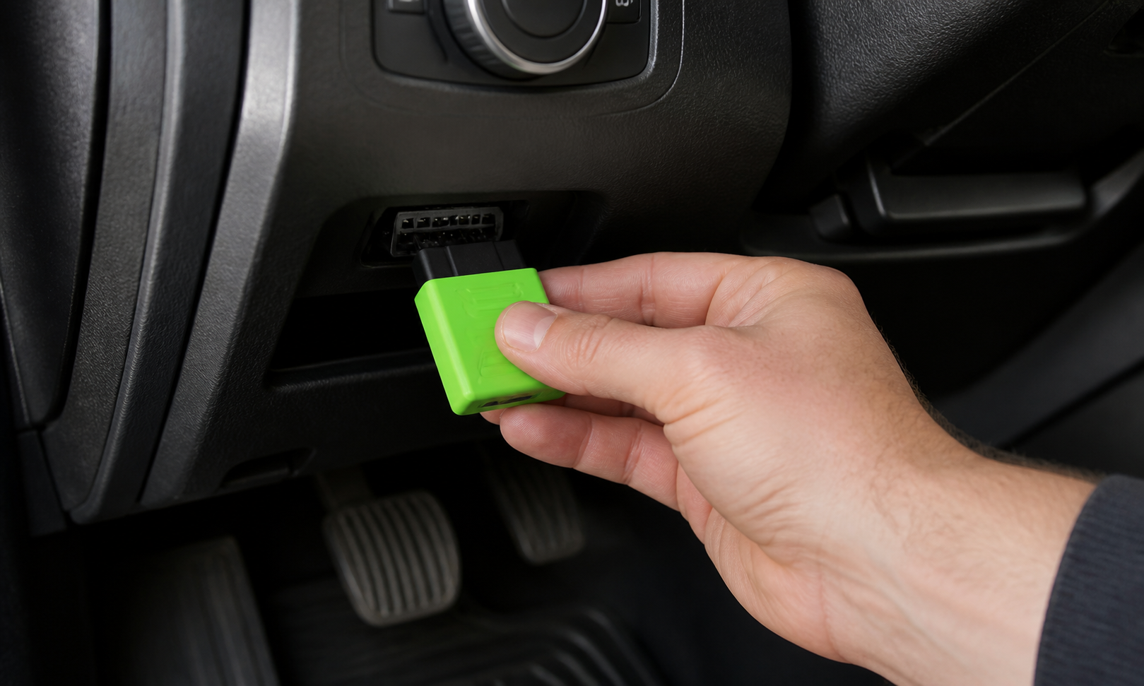 Hand plugging a green OBD2 fuel efficiency chip under a steering wheel
